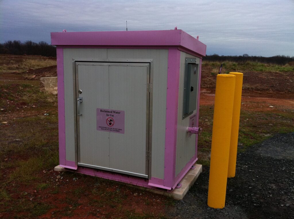 Reclaimed water loading station with custom pink colored trim and pipes and Flowpoint Systems control building, used for reused water distribution to commercial and municipal trucks.