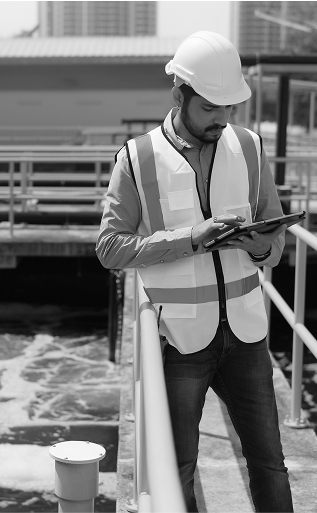 Man in hard hat and vest using tablet at a municipal water treatment facility.